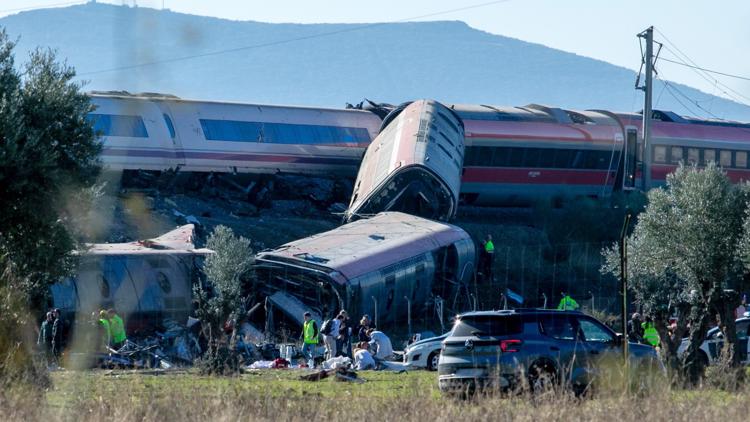 Rescue workers at the scene of a train derailment in Spain, with damaged train cars visible.